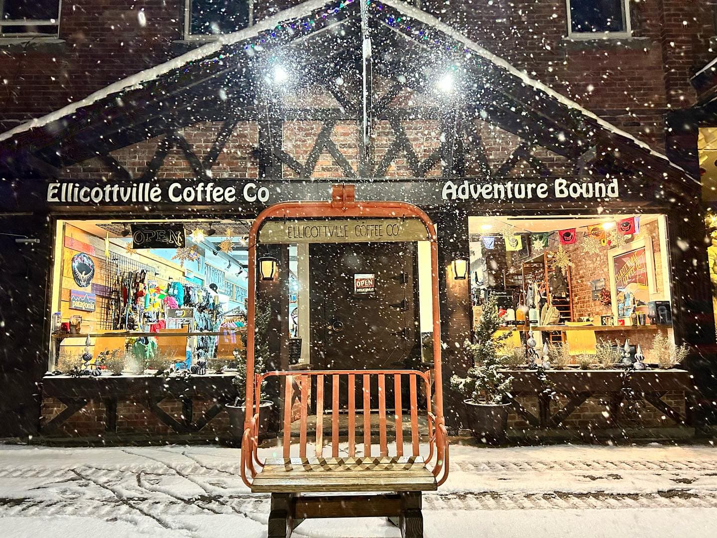 Ellicottville Coffee Co. and Adventure Bound storefront on a snowy night, with a vintage chairlift bench out front