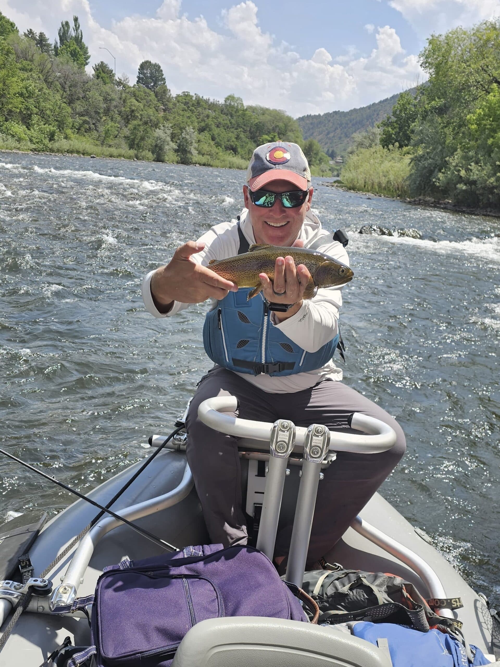John Rounds holding a rainbow trout from a raft on a Colorado river